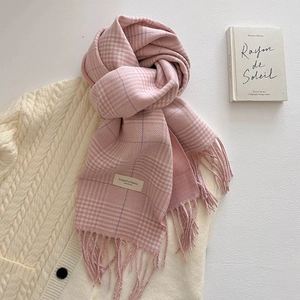 Detail of pink and white plaid scarf with tassels on a cable knit sweater background