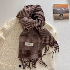Detailed view of the brown plaid scarf featuring thick woven fringe and an elegant label