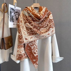 Detail of caramel paisley scarf with tassels draped over a white coat in an elegant setting
