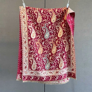 Detailed macro view of vintage paisley pattern on a red cashmere shawl with fringe trim
