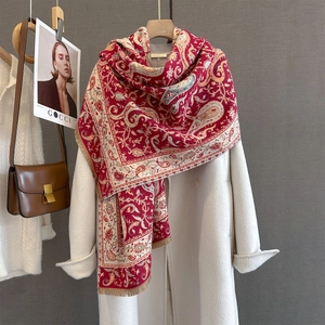 Detail of red paisley scarf with delicate tassels layered on a white cashmere coat