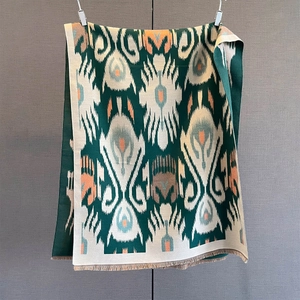 Detail of dark green paisley pashmina scarf with orange ikat pattern and fringe trim