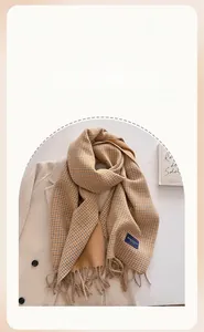 Detailed view of ginger houndstooth knit scarf with tassels layered on a beige wool coat