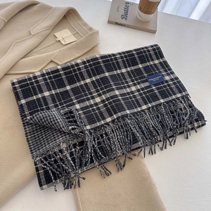 Close-up of thick black and white plaid scarf with long tassels and woven blue label