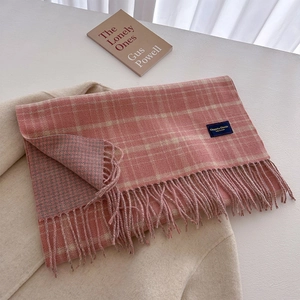 Detail of pink-orange plaid scarf with fringe and woven label on beige coat