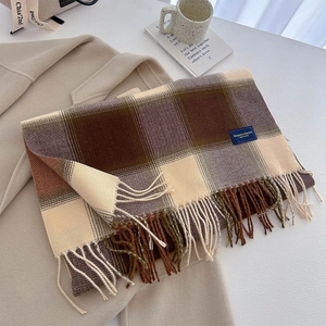 Detail of plaid scarf with fringe and elegant label layered on a beige coat
