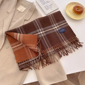 Thick autumn checkered scarf with tassels in brown and orange on a beige wool coat