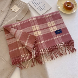 Detail of soft red and white plaid scarf with long tassels on a beige coat surface