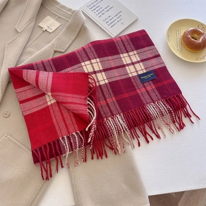 Detail of red plaid scarf with thick tassels and Elegant & Classic label on beige coat