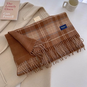 Detail of brown plaid scarf with fringe and label paired with beige coat and coffee mug