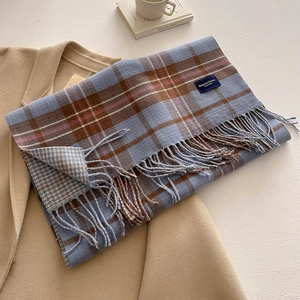 Close-up of classic plaid scarf with fringe on a coat beside a coffee cup and book