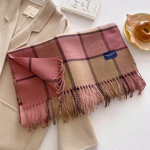 Plaid cashmere-like scarf with tassels over a beige wool coat in a cozy winter setting