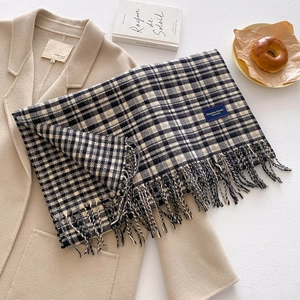 Flat lay of black and white checkered scarf with fringe tassels on beige coat background