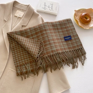 Detail shot of a thick plaid tassel scarf in coffee and grey-green over a beige coat