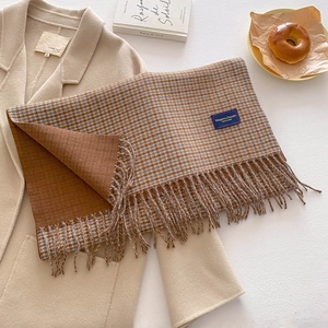Close-up of houndstooth plaid scarf with fringe tassels and a blue label on beige coat