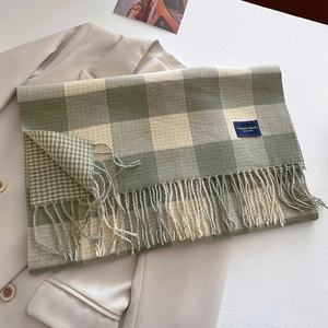 Close-up of green and white plaid scarf featuring thick tassels and woven logo detail