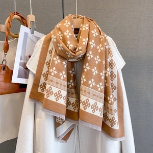 Dettaglio della sciarpa in maglia color cammello con motivi a fiocchi e frange
