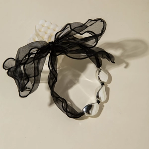 Detail of a large black organza bow necklace with metallic beads on a stone base
