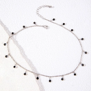 Detail view of silver chain necklace featuring round black charms and lobster clasp