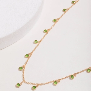 Detail of gold chain necklace featuring bezel-set round green gemstones and minimalist design