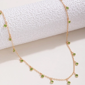 Close-up of a delicate gold chain necklace with round green gemstones and tassel accents