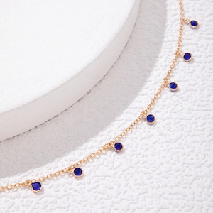 Detail of rose gold chain necklace with blue crystal charms on white background