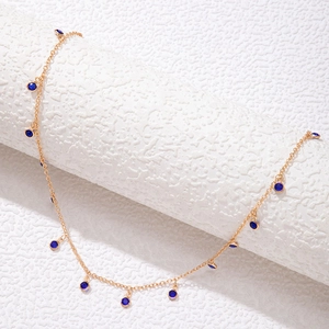Detail of a thin gold chain necklace featuring bezel-set round blue gemstones on texture