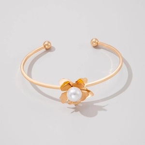 Détail d'un bracelet ouvert doré orné d'un motif floral et d'une perle blanche