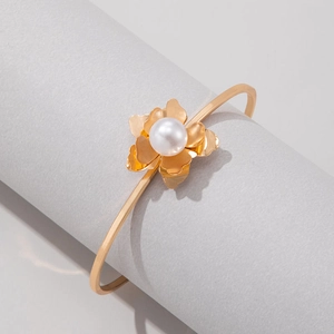 Détail d'un bracelet ouvert doré orné d'une fleur avec perle blanche centrale