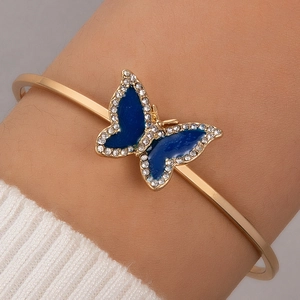 Vue détaillée d'un bracelet doré ouvert avec un papillon en émail bleu et des pierres