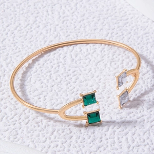 Détail d'un bracelet ouvert doré orné de cristaux carrés vert émeraude et gris fumé