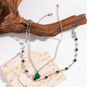 Détails du collier superposé argenté et du bracelet avec pierres précieuses vert émeraude