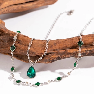 Détail du pendentif goutte émeraude sur chaîne étoilée posée sur du bois naturel
