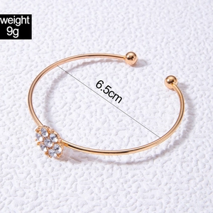Gros plan d'un bracelet ouvert doré à motif floral avec strass et diamètre de 6,5 cm