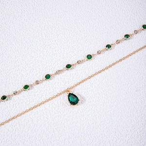 Détail du collier doré double rang avec goutte d'émeraude et chaîne de style tennis
