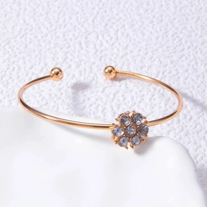 Détail d'un bracelet ouvert doré orné d'une fleur en strass brillants et de perles de métal