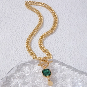 Détail d'un collier chaîne gourmette dorée avec pendentif émeraude et fermoir à bascule