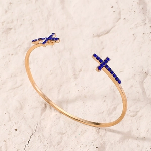 Détail d'un bracelet ouvert doré orné de croix en strass bleus sur fond de pierre