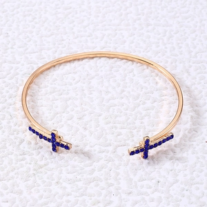 Détail d'un bracelet jonc doré orné de deux croix serties de cristaux bleu foncé