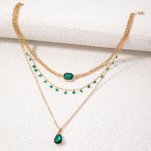 Detail van een drielaagse gouden ketting met smaragdgroene vierkante en druppelstenen