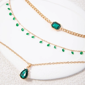Gelaagde gouden ketting met smaragdgroene stenen en vlinder- en hartvormige hangers