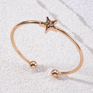 Détail du bracelet ouvert en or rose avec étoile en strass colorés sur fond de pierre