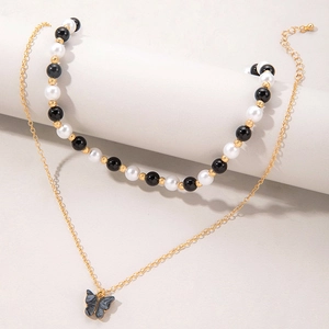 Detail van de goudkleurige gelaagde ketting met zwarte vlinder hanger en kralen