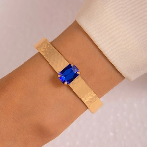 Détail d'un bracelet manchette doré martelé avec un cristal bleu rectangulaire serti à griffes