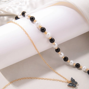 Detail van gelaagde sieraden met zwart-witte parels en een vlinderhanger aan de ketting