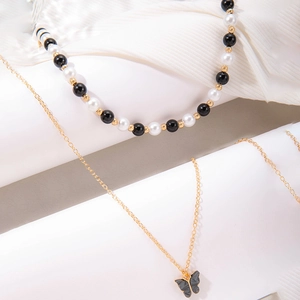 Detail van gelaagde gouden ketting met een vlinderhanger in marmertextuur en kralen