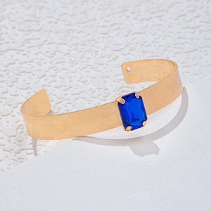 Détail d'un bracelet ouvert doré martelé orné d'une pierre précieuse rectangulaire bleu marine