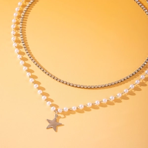 Detail van gelaagde ketting met zilveren sterhanger, parels en glanzende strass-steentjes