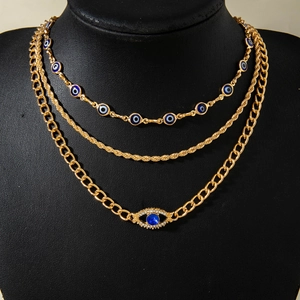 Detail van een goudkleurige drielaagse ketting met blauwe boze oog-bedeltjes en strass-hanger