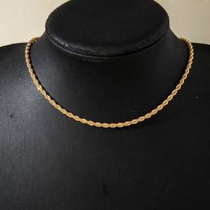 Gedetailleerde close-up van een gouden gedraaide touwketting op zwarte sieradenstand